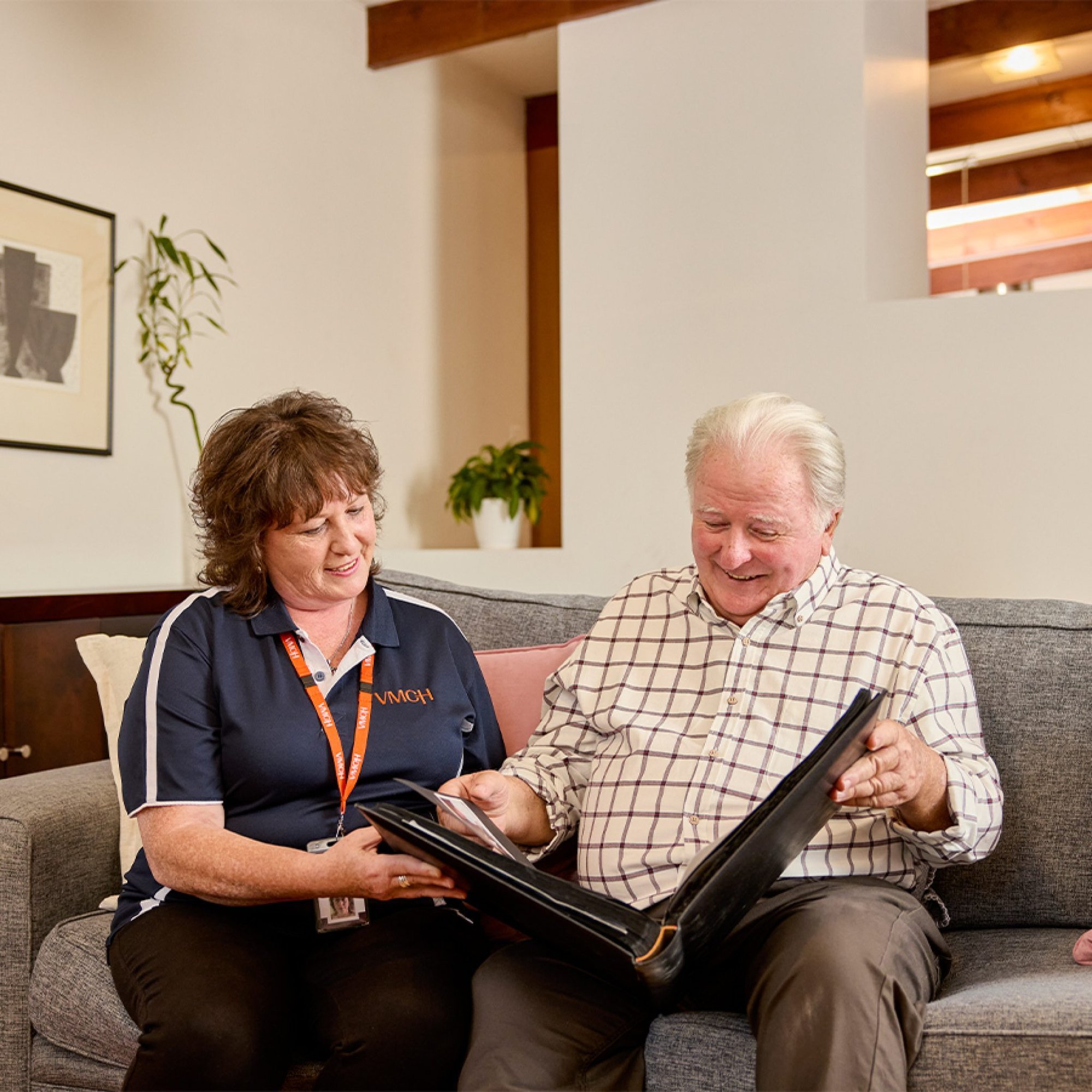 VMCH worker sitting on couch with elderly man looking through binder